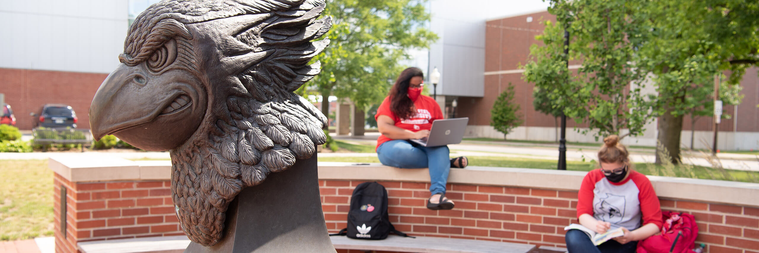 Two students sit on the bench surrounding the Reggie head statue.